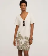 Vestido t-shirt corto de viscolino color crudo, con escote en V y manga corta. Presenta un estampado de follaje en tonos verdes y rosados en el bajo.