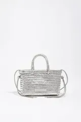 Minibolso estructurado de cuero trenzado color plateado, con asas de mano y correa larga de hombro ajustable. Incluye una pequeña etiqueta de cuero con logotipo grabado en la parte frontal.