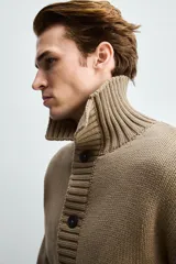 Chaqueta de punto de corte relajado, color marrón, con cuello subido, manga larga y cierre frontal de botones. Presenta acabados en rib en puños y ruedo.