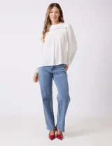 Blusa azul de gasa con pliegues en la parte delantera y detalles de encaje calado. Cuello alto fruncido y mangas largas con puños elastizados. Espalda lisa con abertura tipo gota y botón.