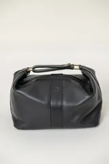 Neceser de cuero negro con cierre superior, manija superior reforzada con herrajes metálicos y detalle de logo grabado en el centro.