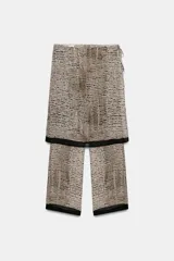 Falda pantalón de tiro bajo con estampado de puntos negros sobre fondo beige. Presenta un diseño de superposición con cierre lateral mediante lazadas y cremallera oculta, finalizando en bordes con detalle de franja negra.