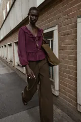 Blusa de color bordó con escote en V profundo adornado con volantes, mangas largas con puños y detalle de peplum en el ruedo. Cuenta con cierre frontal de botones forrados en la misma tela.