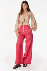 Pantalón de lino blanco de corte ancho y fluido, con cintura alta que incorpora una sobrepretina ancha desmontable con pliegues horizontales.