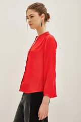 Camisa de satén color rojo, con cuello mao y escote en V, mangas largas con puños elásticos y detalle de frunces en los hombros.