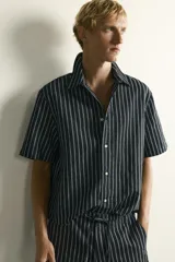 Camisa de corte relajado confeccionada en denim de algodón y lino, con diseño de rayas verticales, cuello solapa y manga corta con cierre frontal de botones.
