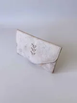 Billetera de cuero con textura rústica y acabado desgastado, presenta un diseño de solapa triangular con un detalle bordado en forma de espiga en el centro.