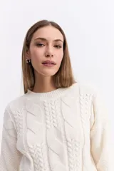 Buzo de punto color blanco, con cuello redondo y diseño de trama combinada con detalles trenzados. Presenta terminaciones tejidas en puños y ruedo.