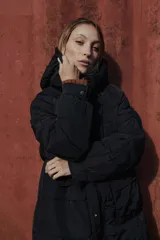 Campera larga acolchonada color marrón, con diseño midi, capucha amplia, cierre frontal con cremallera y broches, y bolsillos delanteros con tapa.