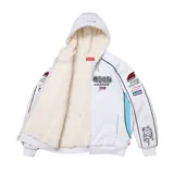 Campera con capucha Supreme estilo racing de color gris melange, con interior de corderito blanco, cierre frontal completo y bolsillos tipo canguro. Presenta múltiples parches y estampados de estilo automovilístico en el pecho y las mangas, además de detalles en color celeste y ribetes negros.