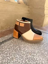 Botinetas de cuero en combinación tricolor de marrón, tostado y beige, con plataforma y taco ancho de madera. Cuenta con detalle de tira con hebilla en el lateral y cierre interno.