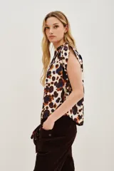 Camisa sin mangas con cuello camisero y botones frontales, confeccionada en tela estampada con patrón animal print en tonos blanco, marrón y azul oscuro.