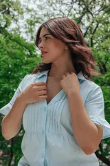 Camisa celeste con cuello mao, mangas cortas con volados y cierre frontal con botones.