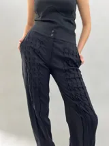 Pantalón tipo babucha confeccionado en lana de oveja, color visón. Presenta un diseño de tiro alto con textura vertical plisada a lo largo de las piernas, cintura con cierre de doble broche y puños elásticos en los tobillos.