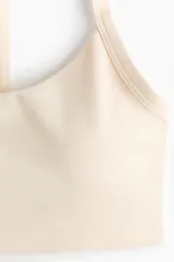 Top deportivo de soporte medio color beige claro con escote redondo y doble tirante en los hombros.