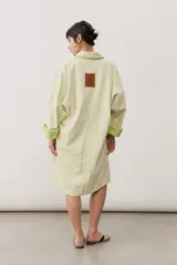 Chaqueta oversize de gabardina color verde claro, con solapa clásica, bolsillos frontales, cierre de botones oscuros y mangas largas con vuelta en tono verde lima vibrante.