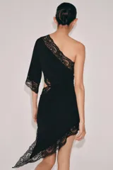 Vestido negro de escote asimétrico con un solo hombro y manga larga ancha. Presenta detalles de encaje negro en el escote, el ruedo asimétrico y un corte 'cut out' en el lateral del torso.