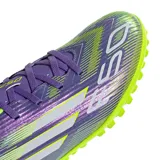 Championes de fútbol Adidas F50 Club para césped sintético, con diseño aerodinámico en tonos violeta y verde lima. Presenta cierre con cordones, suela con tapones pequeños para tracción y el logo F50 estampado en el frente.