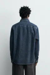 Camisa de corte relajado confeccionada en denim de algodón, con cuello solapa, manga larga con puños abotonados y cierre frontal de botones.