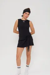 Vestido corto deportivo negro, sin mangas, con cuello redondo y detalle de lazo anudado en la cintura. Presenta el logo 'bk.' estampado en blanco en el pecho.