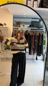 Sweater tejido de punto con diseño a rayas horizontales en tonos amarillo, celeste y marrón. Presenta un cuello polo con escote en V, mangas largas y un corte holgado.