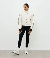 Campera puffer deportiva Get Over, color blanco con detalles de bies en color negro a lo largo de las mangas. Presenta cuello alto con capucha integrada, cierre frontal con botones a presión, bolsillos laterales con cremallera y puños con elásticos.