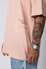Remera blanca de corte oversize con cuello redondo y mangas cortas. Presenta un pequeño estampado tipográfico en la parte inferior frontal y un diseño gráfico de mayor tamaño en la espalda.
