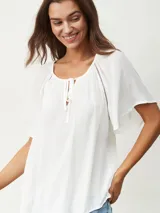 Blusa blanca de manga corta con textura arrugada, escote redondo con abertura en V y lazos ajustables. Presenta detalles de puntilla calada en los hombros.