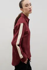 Camisa de corte holgado y largo medio, color negro con detalle de franja lateral en color crema a lo largo de las mangas. Presenta cuello clásico, cierre frontal con botones y tajos laterales en el ruedo.