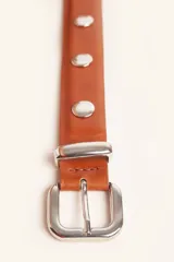 Cinto de cuero color suela con tachas metálicas circulares y hebilla plateada.