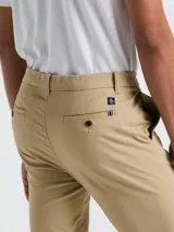 Pantalón chino color beige, con bolsillos delanteros diagonales, cierre y botón en la cintura. Logo bordado a tono.