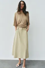 Falda midi de tiro alto color beige, con bolsillos delanteros, cintura con trabillas y cierre frontal con cremallera y ganchos metálicos.