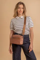 Bandolera de diseño moderno y funcional, confeccionada en nylon color marrón claro. Cuenta con múltiples compartimentos con cierre metálico, herrajes plateados y una correa ancha ajustable con detalle de marca.