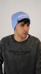 Gorro tipo beanie de tejido acanalado en color celeste, con bordado frontal en color blanco.