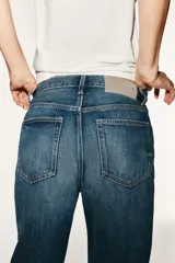 Jeans de tiro medio con corte straight, color azul con efecto lavado y roturas sutiles, cinco bolsillos y cierre frontal con cremallera y botón metálico.