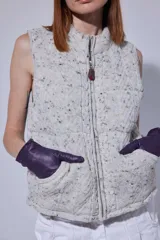 Chaleco tejido de punto con efecto acolchado, cuello alto y cierre frontal con tirador de cuero. Presenta un diseño con cortes horizontales y bolsillos delanteros.