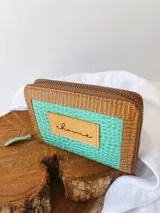 Billetera compacta de cuero con diseño bicolor en turquesa y marrón, con textura tipo reptil. Cuenta con cierre metálico perimetral y parche frontal con el logo de la marca.