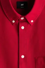 Camisa en algodón Oxford de color rojo con cuello americano, bolsillo superior abierto, mangas largas con puños abotonados y corte relajado.