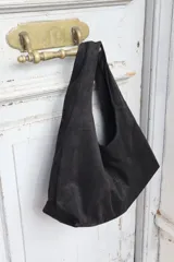 Cartera tipo hobo de gamuza negra, con diseño minimalista y asa integrada.