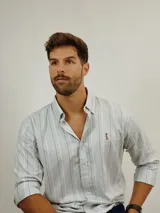 Camisa de manga larga con cuello abotonado, confeccionada en tejido de algodón con estampado de rayas verticales en tonos celestes, blancos y beige. Presenta un pequeño bordado en el pecho.