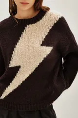 Sweater de punto con diseño de rayo en color crema sobre fondo marrón oscuro, de corte holgado, cuello redondo y mangas largas con puños acanalados.
