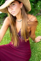 Vestido largo con estampado tie-dye en tonos violeta y fucsia, escote en V con detalles bordados dorados, cut-outs laterales bajo el busto y tirantes finos que se cruzan y atan en la espalda.