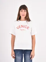 Remera de algodón blanca con cuello redondo y mangas cortas. Presenta un estampado frontal con la palabra 'VENICE' en letras rojas y la frase 'Italy, Amore' en cursiva debajo.
