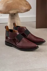 Zapato tipo botineta de cuero color bordó con textura grabada, diseño de punta fina y detalles de elásticos laterales en color negro.