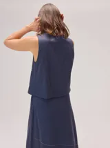 Chaleco negro sin mangas, de corte recto y largo a la cintura, con cuello redondo y cierre frontal oculto.