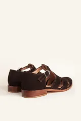 Sandalias de gamuza color marrón, estilo romano con diseño en T, tiras con aberturas laterales y cierre de hebilla metálica en el tobillo. Cuenta con tacón bajo de madera.
