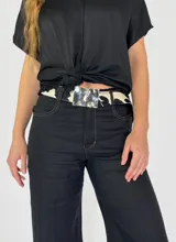 Cinturón con estampado animal print de vaca en blanco y negro, con hebilla cuadrada plateada con diseño abstracto.