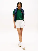 Remera verde de algodón con cuello redondo y corte amplio. Presenta el logo de Tommy Hilfiger en el pecho y un logo oversize en la parte trasera. Tiene mangas cortas con hombros caídos y un parche con logo en la manga.