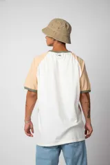 Remera estilo raglán color blanco en el cuerpo, con mangas en tono tostado y ribetes en color verde militar en el cuello y los puños.