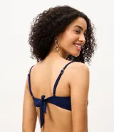 Top de bikini bandeau azul marino confeccionado en microfibra texturizada, con tirantes finos regulables y removibles. Cuenta con un aplique redondo de paja en el centro del busto y copas extraíbles.